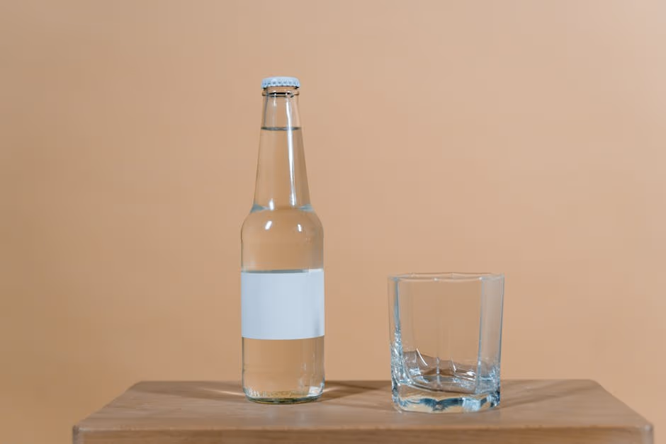 Clear glass bottle and cup on wooden surface with a soft brown background.